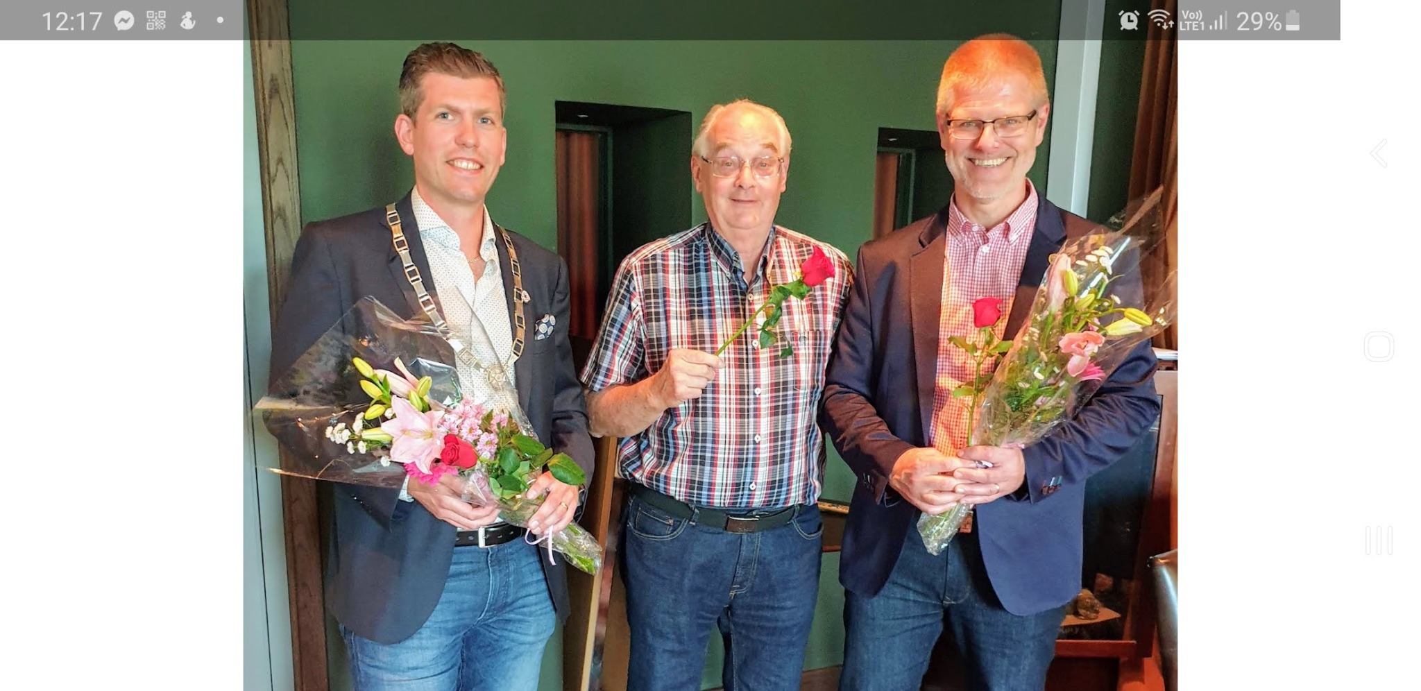 Tre deltagare med blommor och presidentkedja vid ett klubbmöte